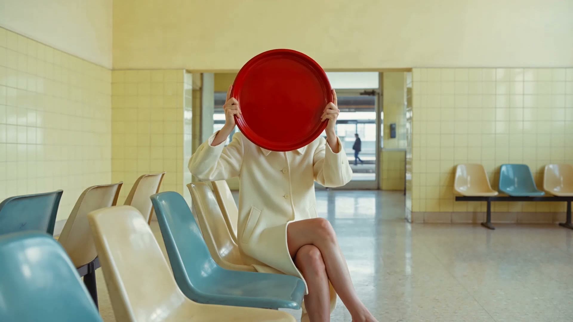 A person in white raising a red tray in a pastel waiting room