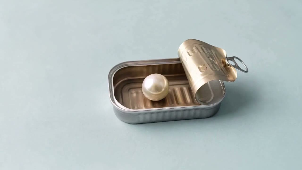 A pearl in an open sardine tin on a pale blue surface